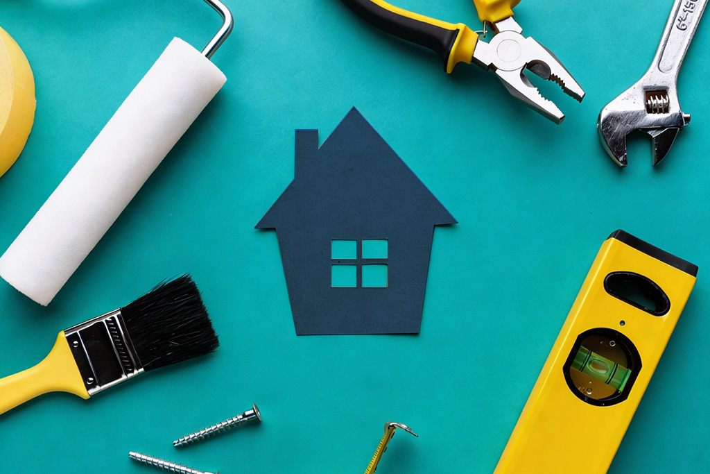 Paint roller, brush, pliers, wrench and level around a paper house