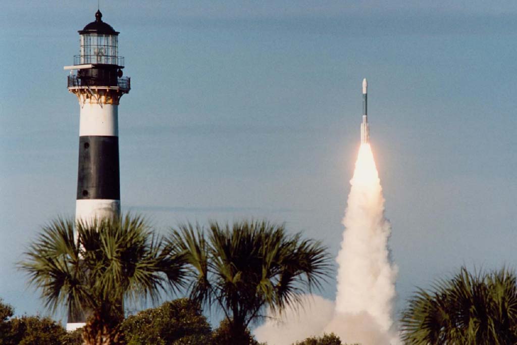 Cape Canaveral lighthouse with a rocket launching behind palm trees on the North Space Coast